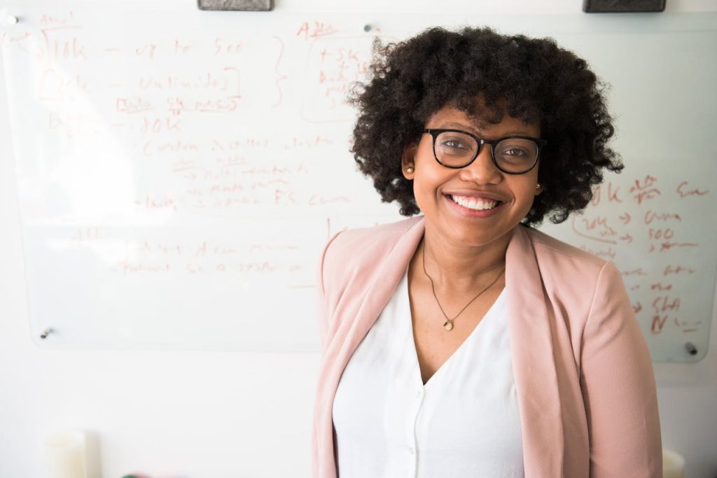 Smiling businesswoman with glasses and afro hairstyle in an office setting.